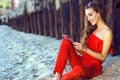 Charming smiling young woman sitting on the beach at the old rusty piles and talking via video connection on her tab