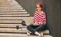 Student girl in earphones sits outside on staircase with laptop, notebooks and takeaway coffee Royalty Free Stock Photo