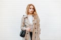 Charming stylish young woman in trendy spring coat in white t-shirt with black fashionable leather bag