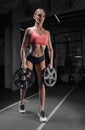 Charming tall athlete posing in the gym with a weight plate. The concept of sports, bodybuilding, fitness, aerobics, stretching