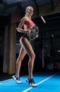 Charming tall athlete posing in the gym with a weight plate. The concept of sports, bodybuilding, fitness, aerobics, stretching