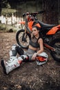 Sensual tattooed racer girl wearing motocross outfit with semi naked torso sitting next to her bike in the woods Royalty Free Stock Photo