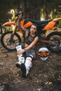 Sensual tattooed racer girl wearing motocross outfit with semi naked torso sitting next to her bike in the woods Royalty Free Stock Photo