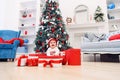 Charming toddler girl holds white christmas gift box with red ribbon. Funny cute baby weared in festive clothes in Royalty Free Stock Photo