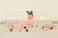 Charming toddler girl sitting on Christmas decorations bed and wearing striped long sleeve baby sleeper and festive deer horns,