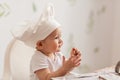 Infant cook baby portrait wearing chef hat playing with dough at kitchen table. Royalty Free Stock Photo