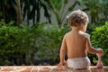 A charming toddler sits on the steps of a house in the sunlight. back view