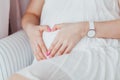 Charming tummy which the pregnant woman in a white dress embraces. The pregnant girl with pink manicure embracing belly Royalty Free Stock Photo