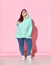 Charming voluptuous lady in stylish hoodie and glasses posing leaning on one leg and touching strand of her long red hair Royalty Free Stock Photo