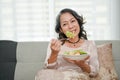 Wellbeing 60s retired Asian woman eating healthy salad while relaxing in her living room Royalty Free Stock Photo