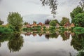 Charming wide canal next to rustic houses with green bushes and trees reflected on the water in cloudy day at Drimmelen.