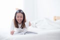 Charming woman lying on bed reading a book and holding coffee cup looking into camera in bedroom Royalty Free Stock Photo