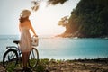 Charming woman in white dress walking bicycle enjoying blue sea.