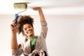 A charming young African woman smiles and holds a roller for painting. Attractive cute mixed race girl paints the walls Royalty Free Stock Photo