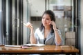 Charming young asian businesswoman sitting in bright modern office and talking on mobile phone Royalty Free Stock Photo