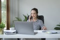 Charming young asian businesswoman sitting in bright modern office and talking on mobile phone Royalty Free Stock Photo