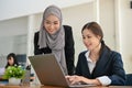 Charming young Asian businesswoman working on the project on laptop with her Muslim colleague Royalty Free Stock Photo