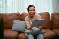 Charming young Asian female enjoys using a digital tablet while relaxing in her home living room Royalty Free Stock Photo