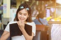 Charming young Asian woman in white shirt sitting at cooffee shop, smiling and writing on a black book for shot note in her hand Royalty Free Stock Photo