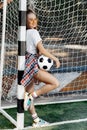 Charming young blonde hipster girl posing with soccer ball in front of goal post at the stadium. Freedom concept. Royalty Free Stock Photo