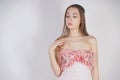 A charming young caucasian girl stands in a pink long prom dress with flower petals on her chest and poses on a white background i Royalty Free Stock Photo