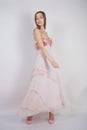 A charming young caucasian girl stands in a pink long prom dress with flower petals on her chest and poses on a white background i
