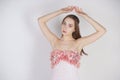 A charming young caucasian girl stands in a pink long prom dress with flower petals on her chest and poses on a white background i