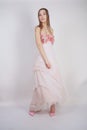 A charming young caucasian girl stands in a pink long prom dress with flower petals on her chest and poses on a white background i Royalty Free Stock Photo