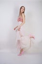 A charming young caucasian girl stands in a pink long prom dress with flower petals on her chest and poses on a white background i Royalty Free Stock Photo