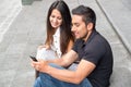 Charming young couple sitting on building steps using mobile phone and interacting happily, urban tourist concept