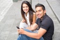 Charming young couple sitting on building steps using mobile phone and interacting happily, urban tourist concept