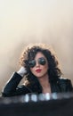 Charming young curly brunette woman with sunglasses and black leather jacket against wall. gorgeous young woman Royalty Free Stock Photo