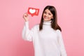 Charming young girl holding heart like icon of social media and looking at camera with toothy smile. Royalty Free Stock Photo