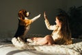 Charming young girl lying on sofa, looking at beagle dog and gives high five. Smiling cute child resting with puppy in sunny morni Royalty Free Stock Photo