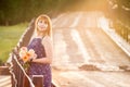 Charming young girl standing on a rustic bridge at dawn sun with a bouquet of roses