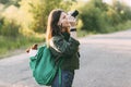 A charming young girl walks in nature, holding a backpack on her shoulder, from which her dog looks out, and holding a camera in Royalty Free Stock Photo