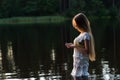 Charming young girl in white dress standing in water on sunset