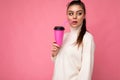 Charming young happy thougthful brunette woman wearing stylish clothes isolated over colourful background wall holding