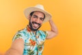 charming young Latino American man in Hawaiian clothes takes a selfie orange background medium closeup studio shot