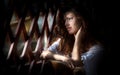 Charming young light brown hair woman looking through wooden grid. gorgeous young woman with long curly hair staying in rays