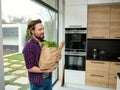 Charming young man enters the kitchen holding paper craft eco bag with food. Handsome guy with cardboard sack full of healthy food Royalty Free Stock Photo