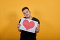 Charming young man wearing black shirt keeping picture of heart, smiling.