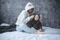 Charming young mother and her daughter are sitting among blankets , both of them in hoodies with bear faces on hoods.