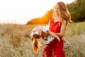 Young mother in a red dress is circling in her arms a little daughter at sunset in the field
