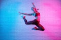 Charming young slim gymnast woman in sports clothing exercises in against brick wall in neon lights. Flexible muscular Royalty Free Stock Photo