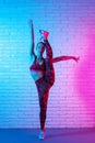 Charming young slim gymnast woman in sports clothing stretching in front of brick wall in neon lights. Flexible muscular Royalty Free Stock Photo