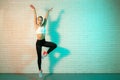 Charming young slim gymnast woman in sports clothing stretching in front of brick wall in neon lights. Flexible muscular Royalty Free Stock Photo