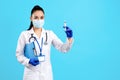 Charming young woman doctor with stethoscope and mask holding clipboard and syringe over blue background. Royalty Free Stock Photo