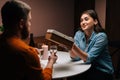 Charming young woman giving wrapped box with gift to man sitting at table with candles on birthday or Valentines Day. Royalty Free Stock Photo