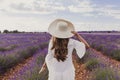 Charming Young woman with a hat and white dress in a purple lavender field at sunset. LIfestyle outdoors. Back view